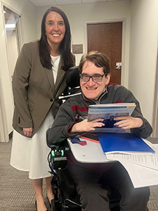 A woman stands behind a man in a motorized wheelchair and smile as they pose with copies of Kindred Stories to hand out to legislators during Tennessee's Disability Day on the Hill.
